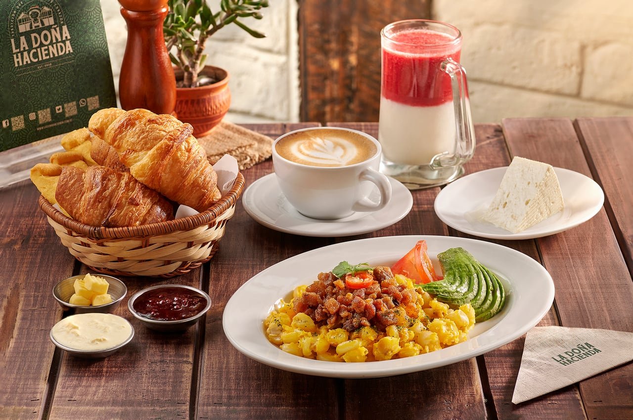 Desayuno tradicional con huevos revueltos, aguacate y tomate, canasta de pan, café y jugo, en La Doña Hacienda