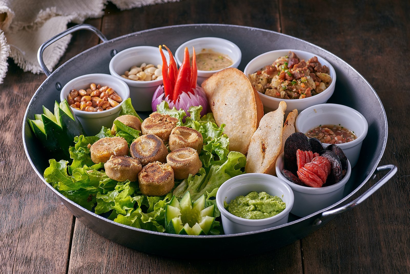 Piqueo para compartir con tortillas de maíz doradas, chifles, ensalada de papa con tocino, guacamole y encurtidos, servido en sartén de hierro en La Doña Hacienda