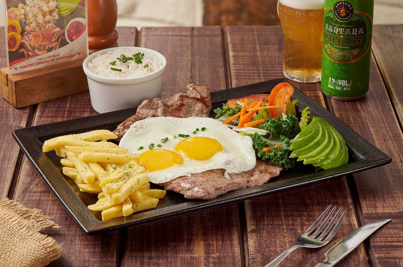 Churrasco ecuatoriano con huevos fritos, papas fritas, arroz, aguacate y ensalada, con cerveza, en La Doña Hacienda