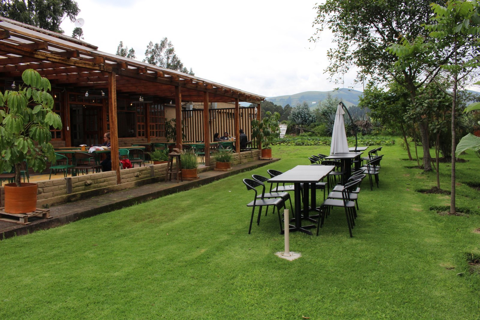 Terraza cubierta con mesas de madera junto a un jardín con huerto en La Doña Hacienda, con las montañas al fondo